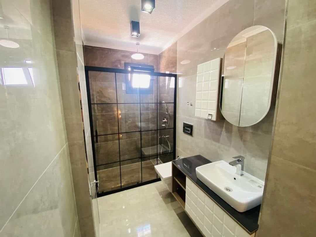 Yuvarlak aynalı, siyah çerçeveli duşlu banyo